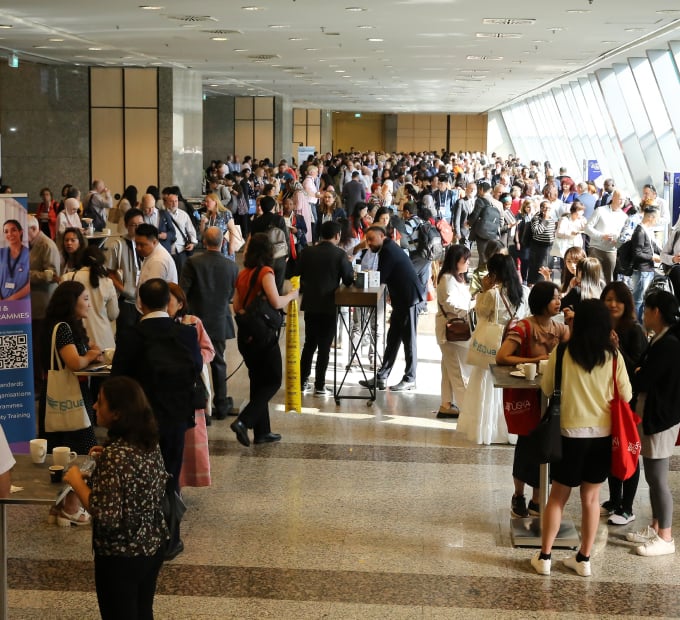 Attendees gather and network in busy conference lobby with posters and banners.