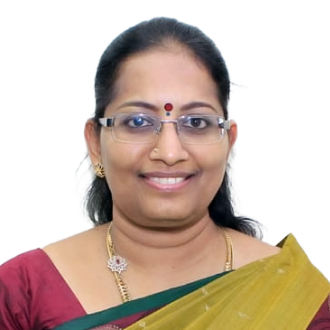 Anuradha Pichumani in a maroon blouse and yellow saree with green border, wearing gold jewelry against a black background.