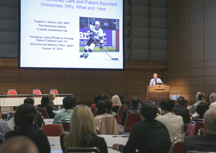 Speaker presents on patient-centered care and PROMs at ISQua 2016 workshop in Tokyo, featuring a slide with a hockey player image. Audience seated in a formal conference setting.