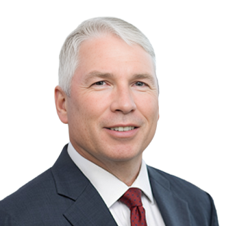 Duncan Inverarity in a dark blue suit and red patterned tie, posing formally against a black background.