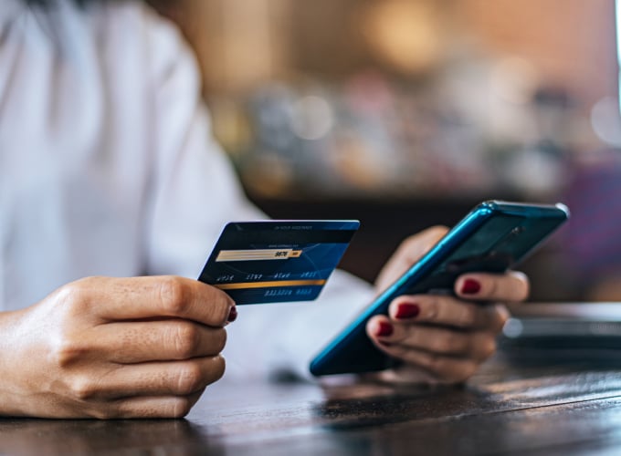 A person holding a credit card and using a smartphone to make a purchase.