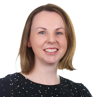Orla Corcoran with shoulder-length light brown hair, wearing a black shirt with white polka dots, posing against a black background.