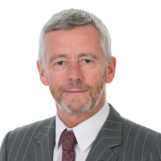 Philip Crowley in a grey pinstripe suit with red patterned tie, posing formally against a black background.