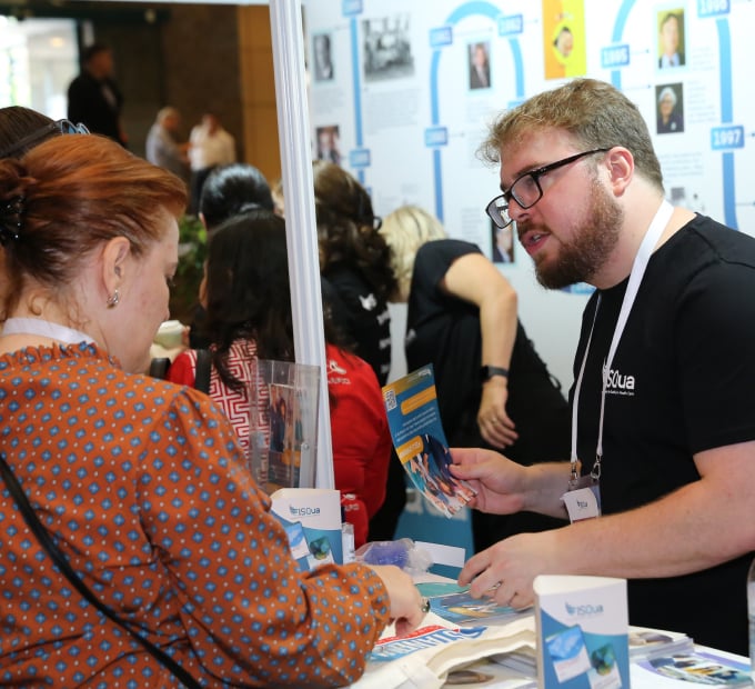 Attendees engage at ISQua conference booth with brochures and timeline display.
