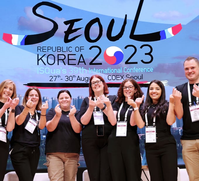 Six smiling conference attendees making finger hearts in front of a Seoul banner.