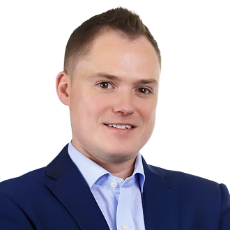 Simon Donohoe in a blue suit and light blue shirt, posing against a black background.