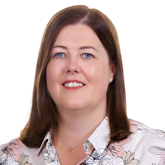 Sinead McArdle with shoulder-length brown hair, wearing a white floral blouse and pendant necklace, posing against a black background.