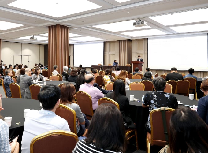 A full room of people seated and listening to a speaker at a conference.