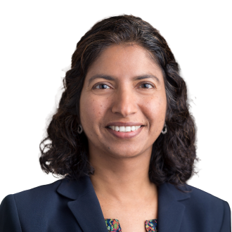 Ulfat Shaikh in a navy blazer and patterned top, smiling warmly against a black background.