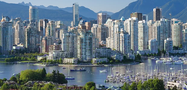 Vancouver cityscape with marina in foreground, high-rise buildings, and mountains in the background.