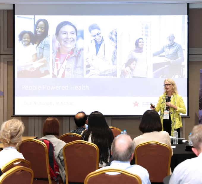 A woman presenting on "People Powered Health" to an audience at a conference.