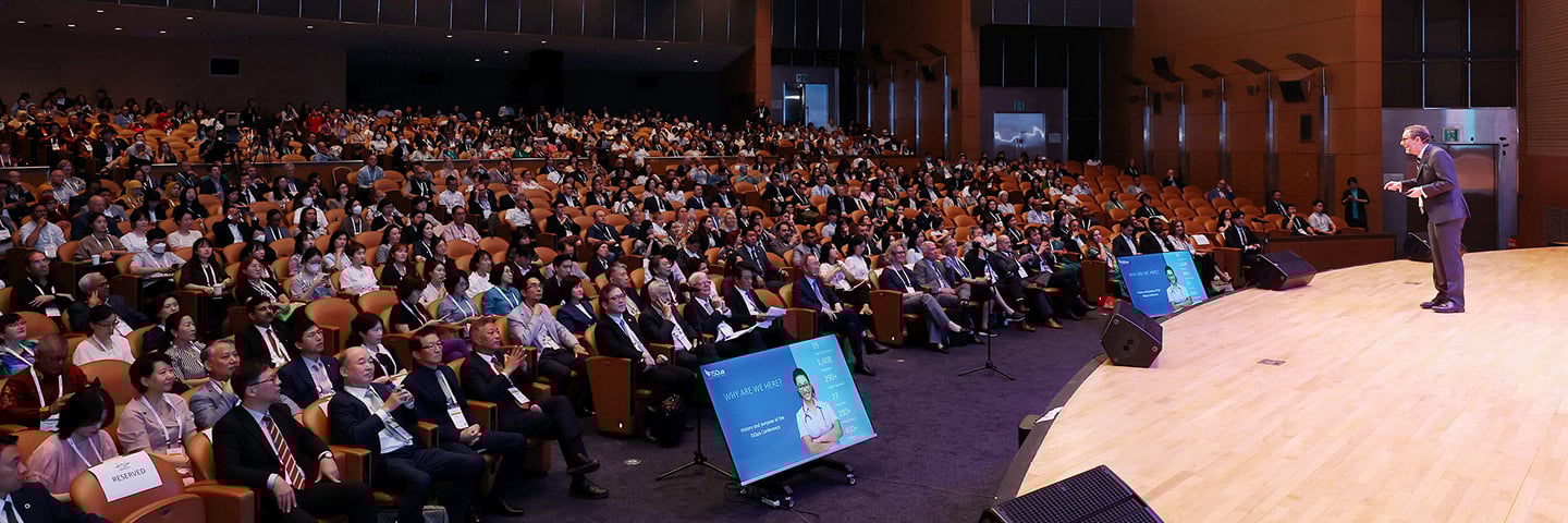 A presenter on a stage speaking to a large audience in a theater.